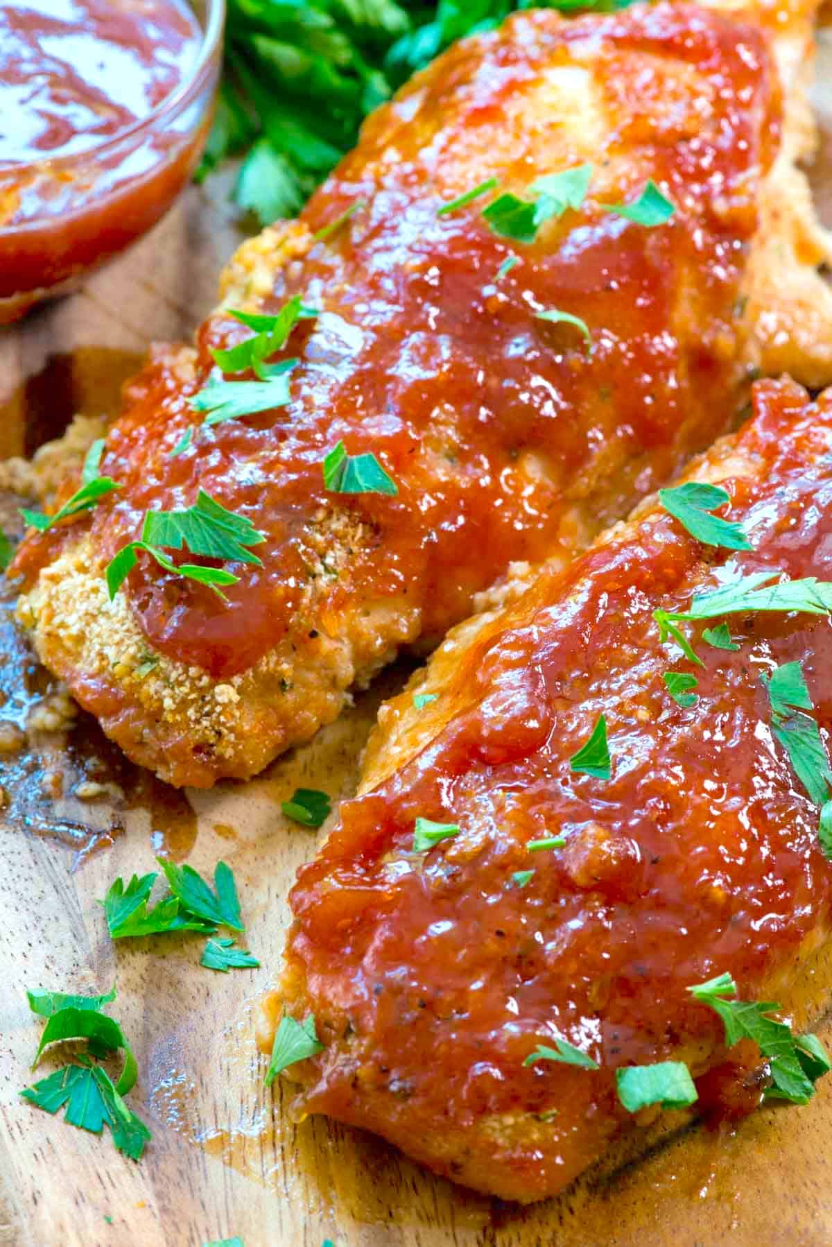 sliced chicken on a cutting board with red sauce and garnish on top.