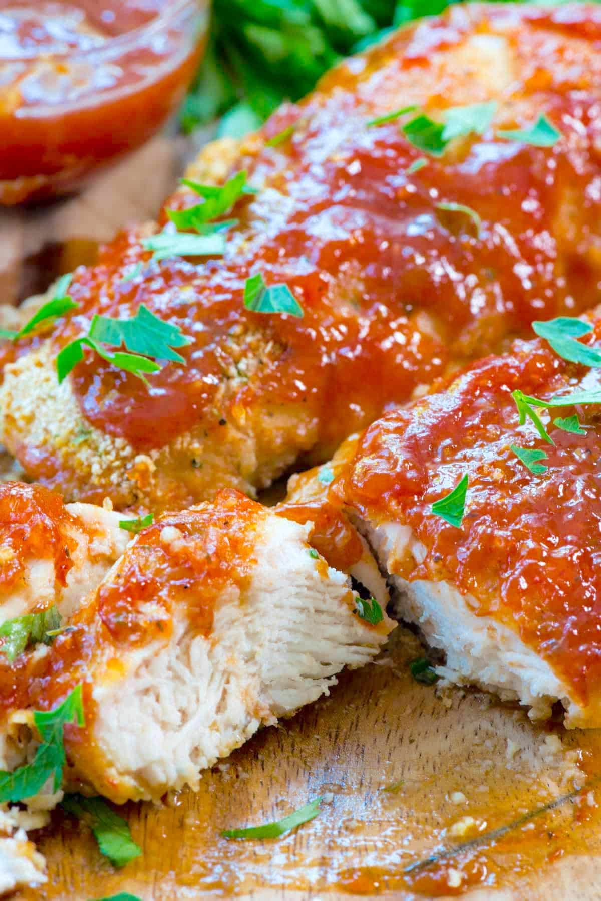 sliced chicken on a cutting board with red sauce and garnish on top.