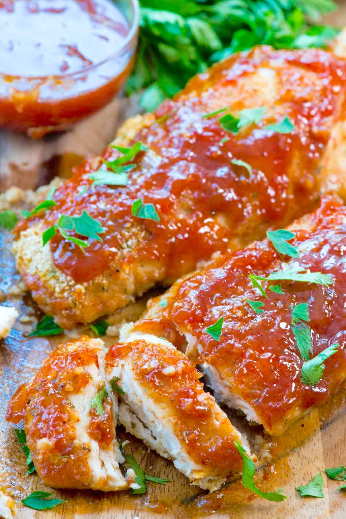 sliced chicken on a cutting board with red sauce and garnish on top.