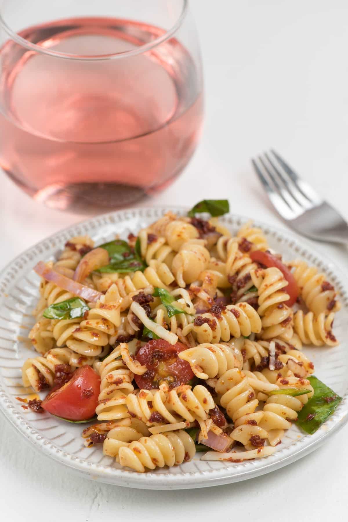 salad mixed with tomatoes and cheese on a grey plate next to a fork and red drink.