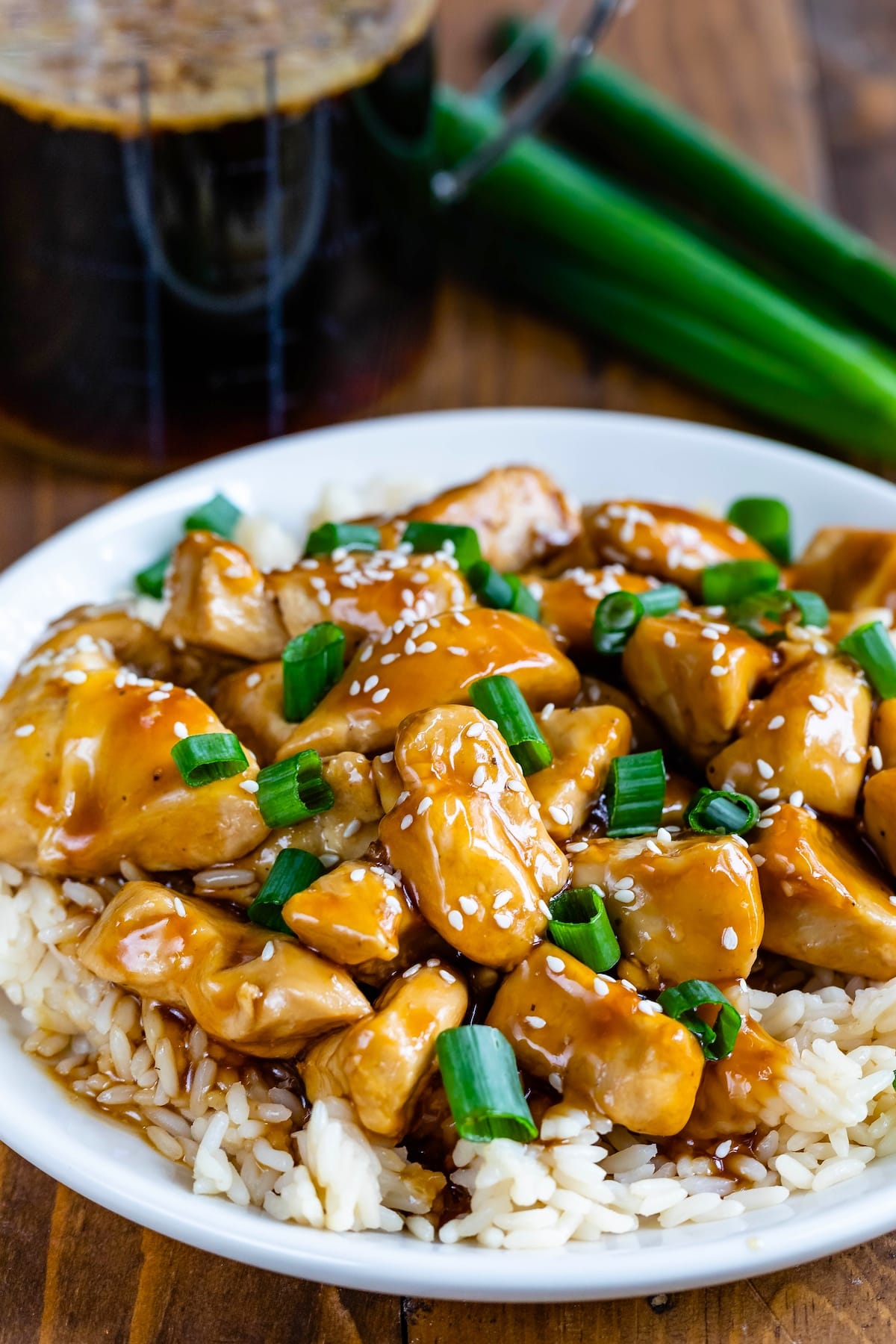 teriyaki chicken sitting on top of rice on a white plate with teriyaki sauce in the background.