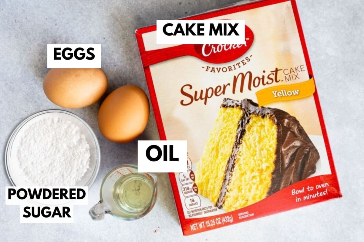 A box of yellow cake mix, two eggs, a bowl of powdered sugar, and a cup of oil are arranged on a light surface—perfect for making Cake Mix Crinkle Cookies. Each ingredient is labeled with bold text.