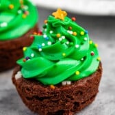 brownie bite on a grey board with green frosting and sprinkles on top replicating a christmas tree and ornaments.