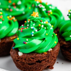 brownie bite on a white plate with green frosting and sprinkles on top replicating a christmas tree and ornaments.