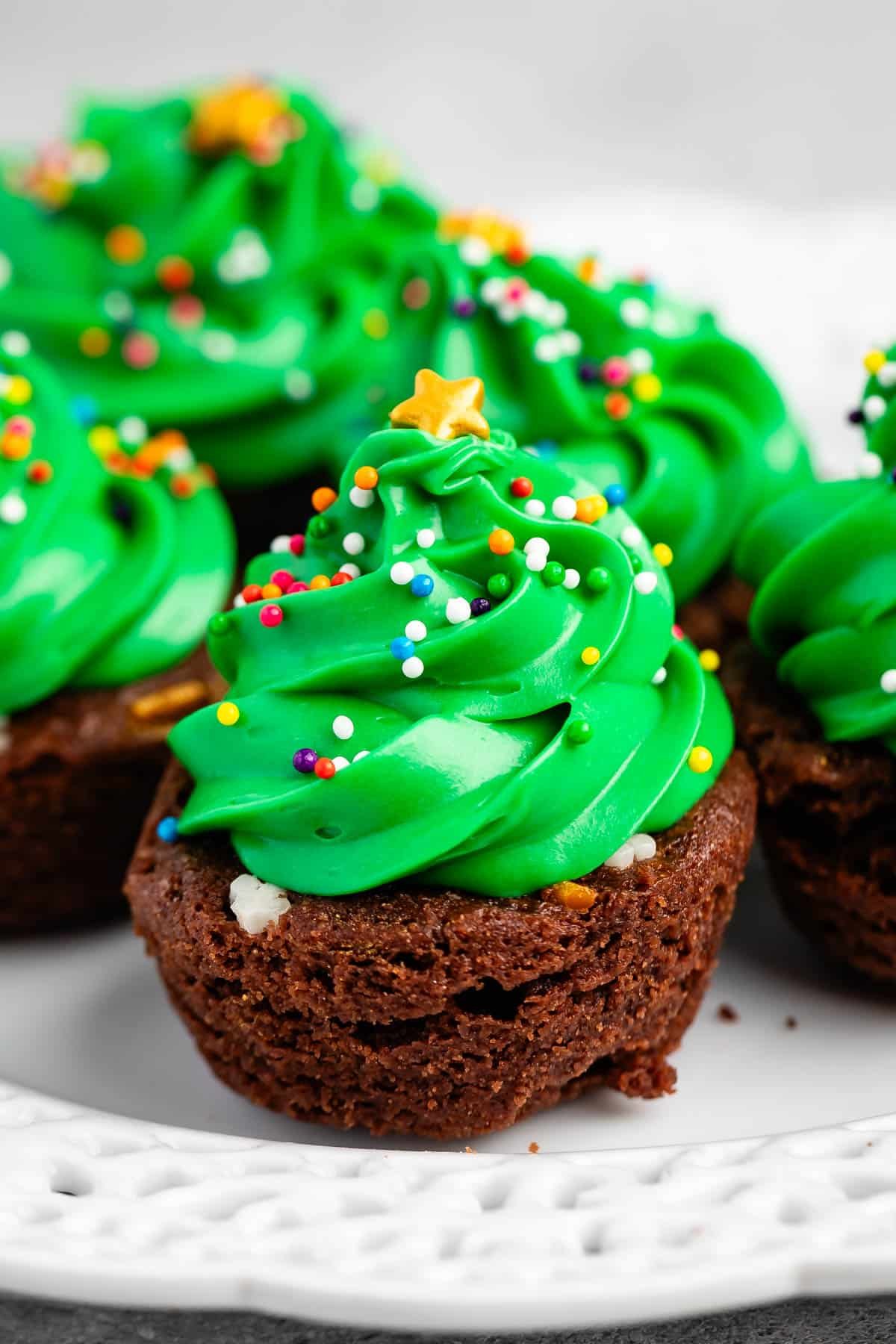 brownie bite on a white plate with green frosting and sprinkles on top replicating a christmas tree and ornaments.