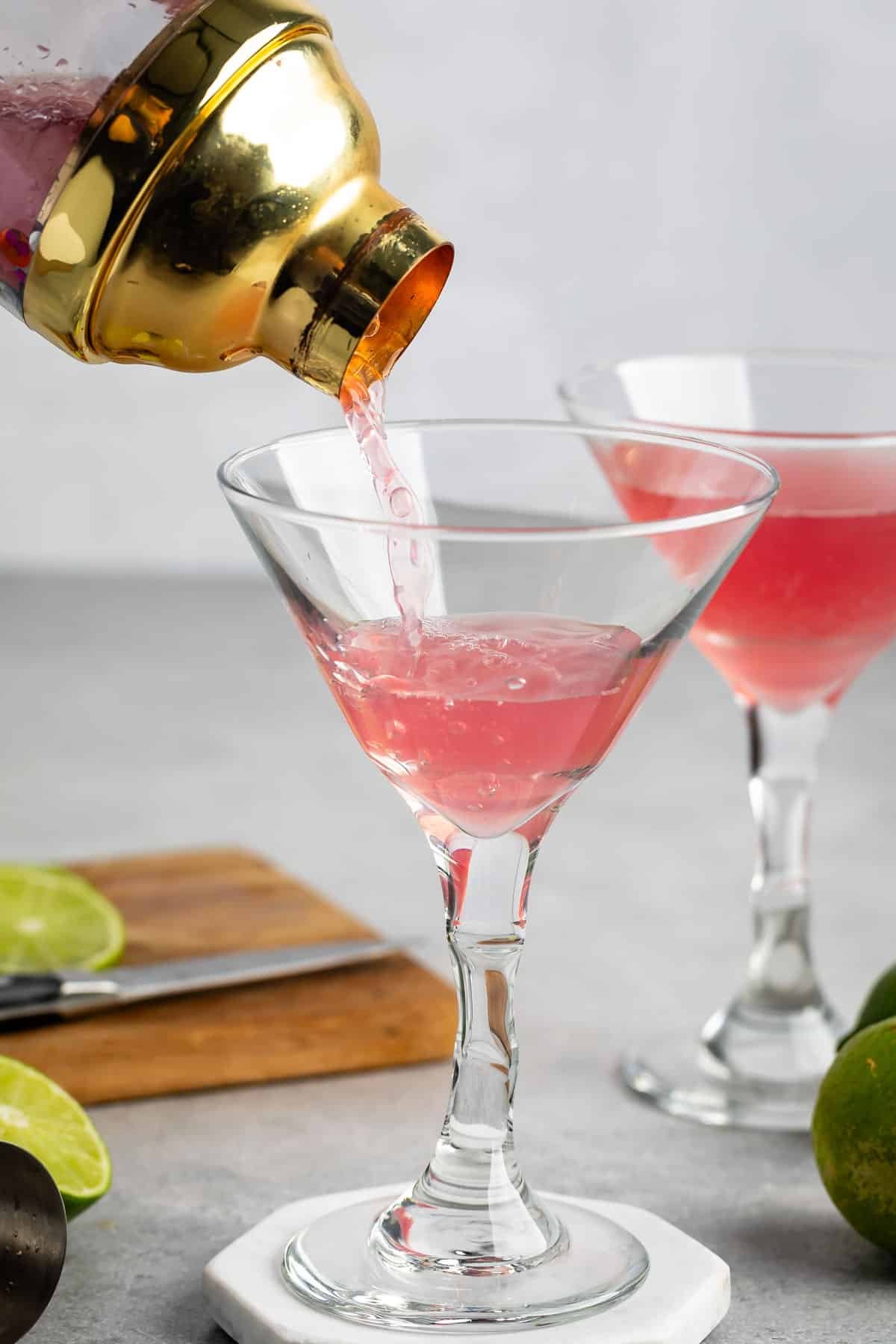 Cosmopolitan drink being poured into the clear glass by the gold shaker.