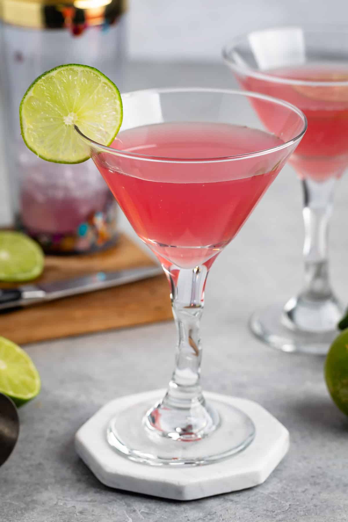 pink drink in a clear glass with a sliced lime on the edge.