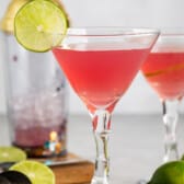 pink drink in a clear glass with a sliced lime on the edge.