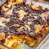 French toast in a square clear pan with chocolate chips and powdered sugar sprinkled on top.