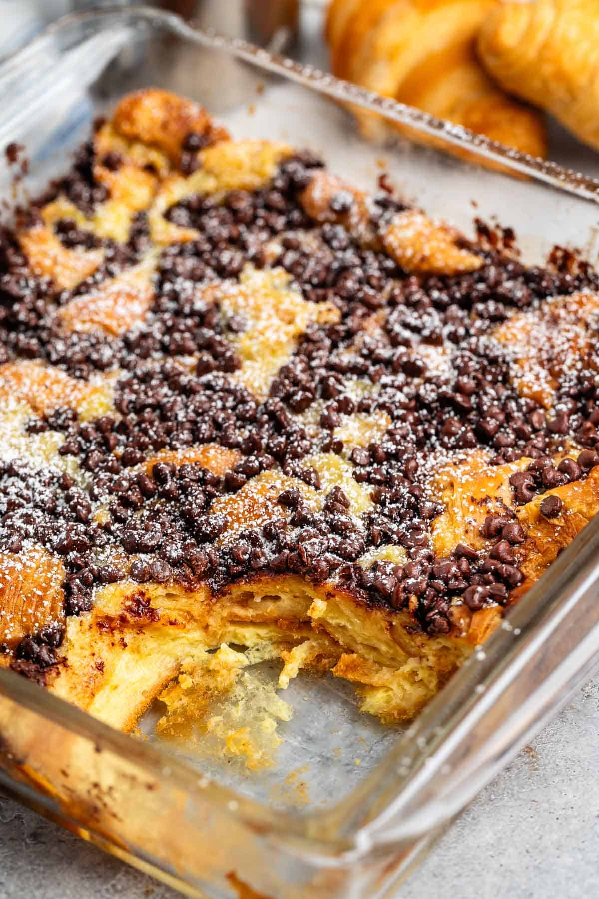 French toast in a square clear pan with chocolate chips and powdered sugar sprinkled on top.