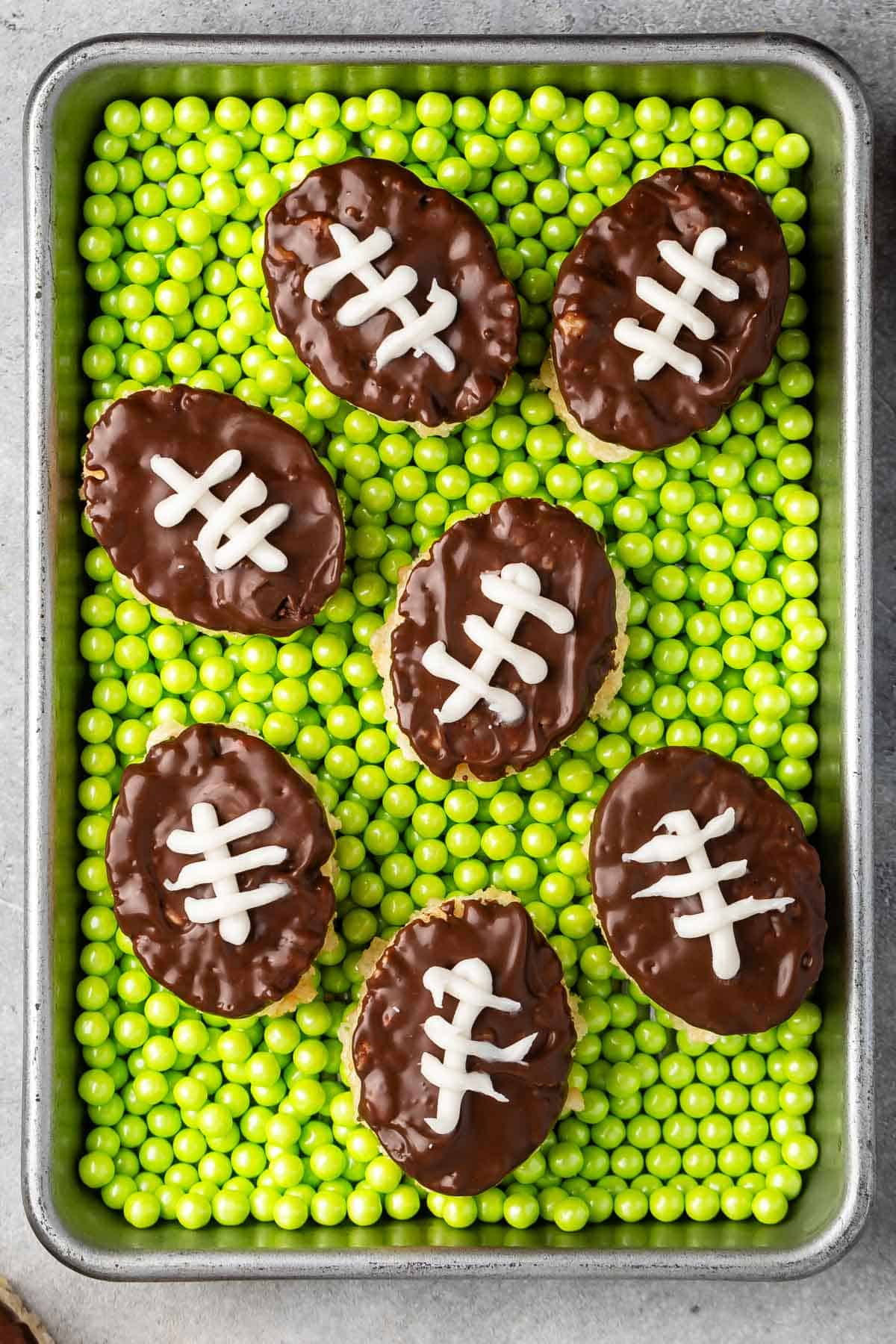 mini Rice Krispie treats in the shape on footballs with brown and white frosting on top to resembles a football on a field.