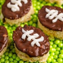 mini Rice Krispie treats in the shape on footballs with brown and white frosting on top to resembles a football on a field.