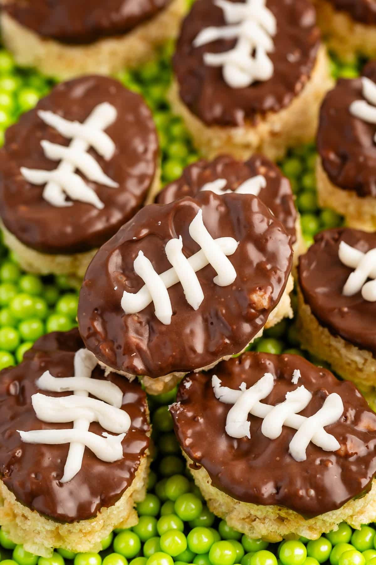 mini Rice Krispie treats in the shape on footballs with brown and white frosting on top to resembles a football on a field.