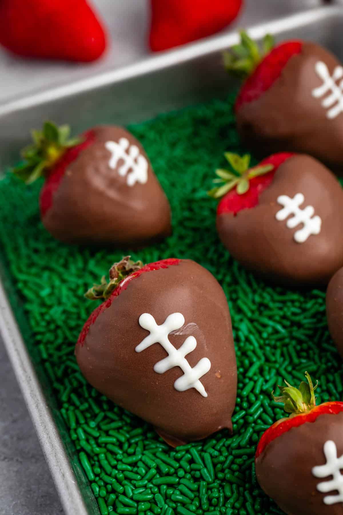 chocolate covered strawberries with white laces drawn on top with green sprinkles underneath.