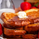stacked French toast this covered in syrup and butter while be surrounded by strawberries.