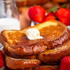 stacked French toast this covered in syrup and butter while be surrounded by strawberries.