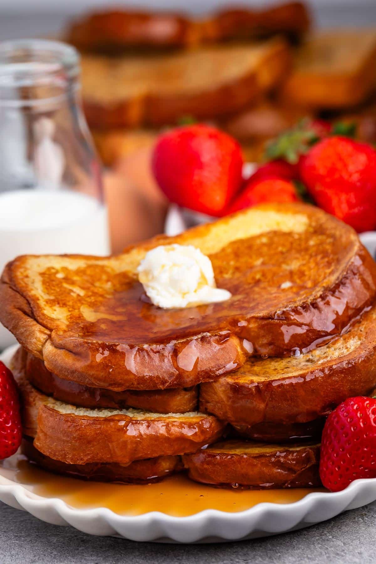 stacked French toast this covered in syrup and butter while be surrounded by strawberries.