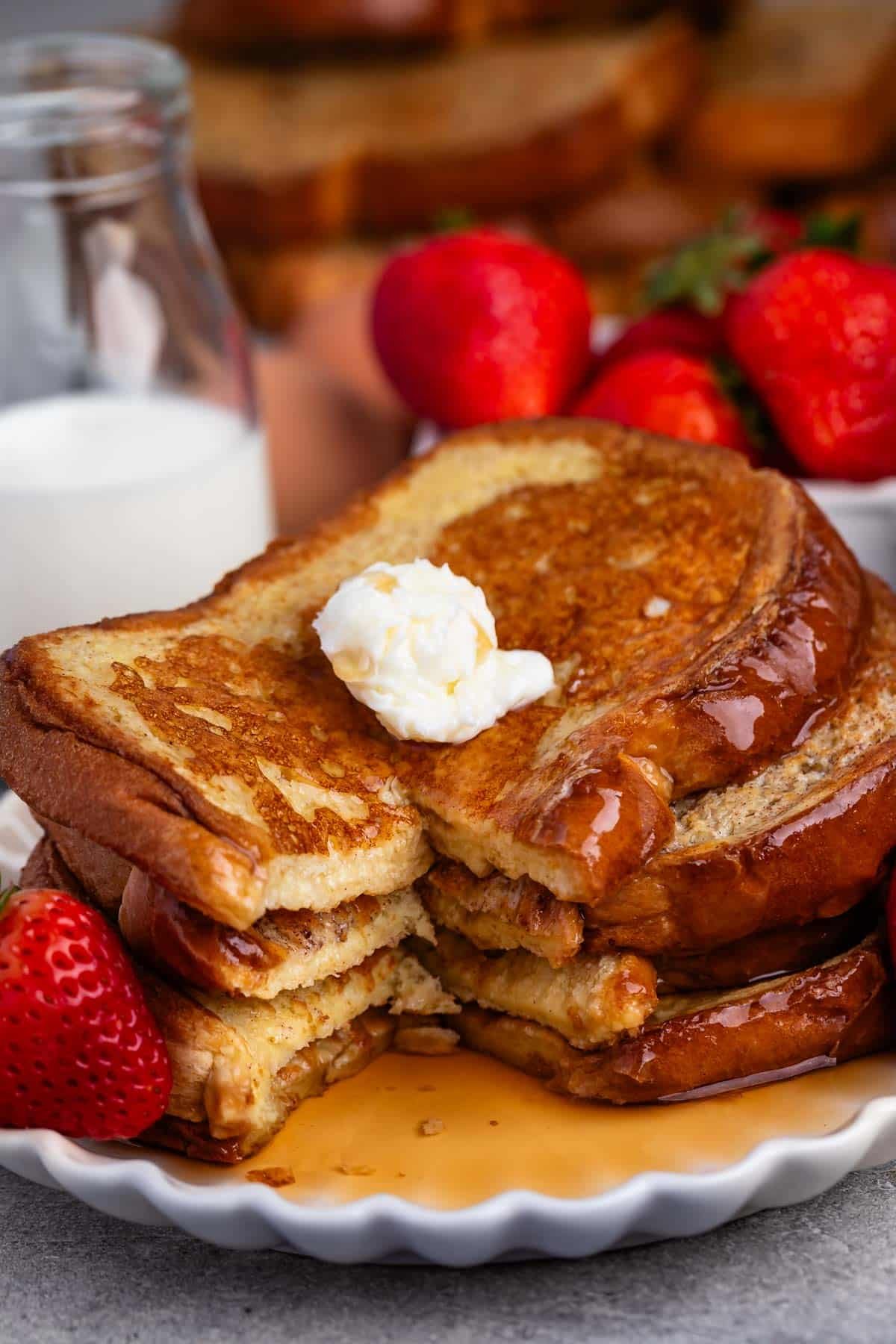 stacked French toast this covered in syrup and butter while be surrounded by strawberries.