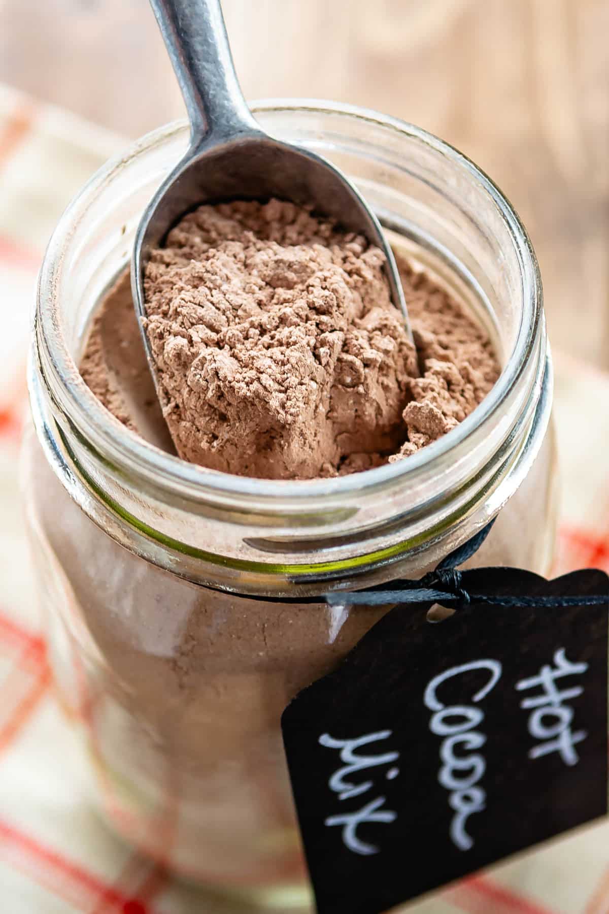 hot chocolate mix in a clear mason jar with a spoon being dipped in the jar with a tag around the rim saying hot chocolate mix.