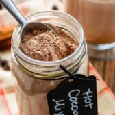 hot chocolate mix in a clear mason jar with a spoon being dipped in the jar with a tag around the rim saying hot chocolate mix.