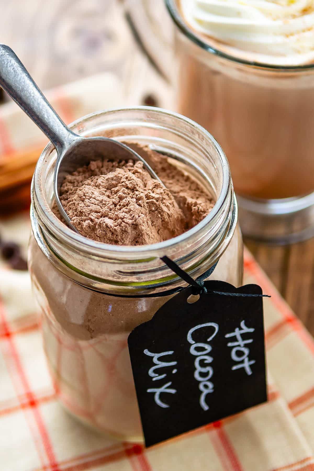 hot chocolate mix in a clear mason jar with a spoon being dipped in the jar with a tag around the rim saying hot chocolate mix.