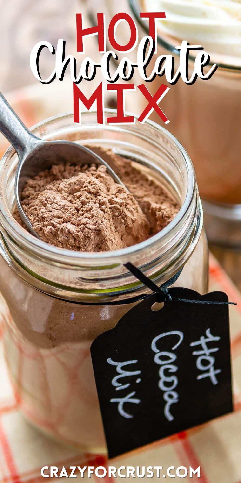 hot chocolate mix in a clear mason jar with a spoon being dipped in the jar with a tag around the rim saying hot chocolate mix with words on the image.