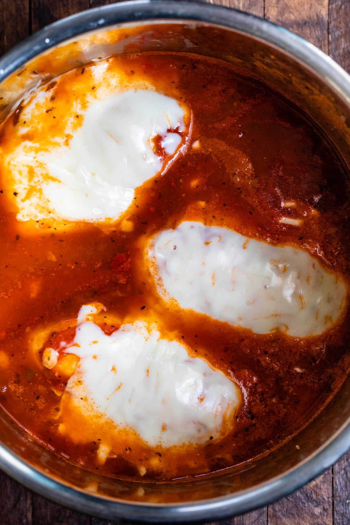 three chicken breasts covered in cheese in a sauce pan with red sauce all around. them