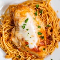 chicken breast on top of spaghetti on a white plate.