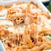 baked penne being scooped out of a teal pan with a silver spoon.