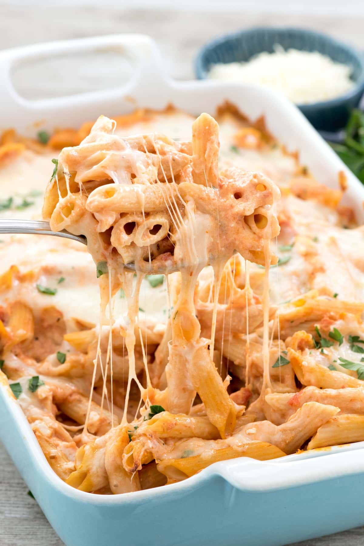 baked penne being scooped out of a teal pan with a silver spoon.
