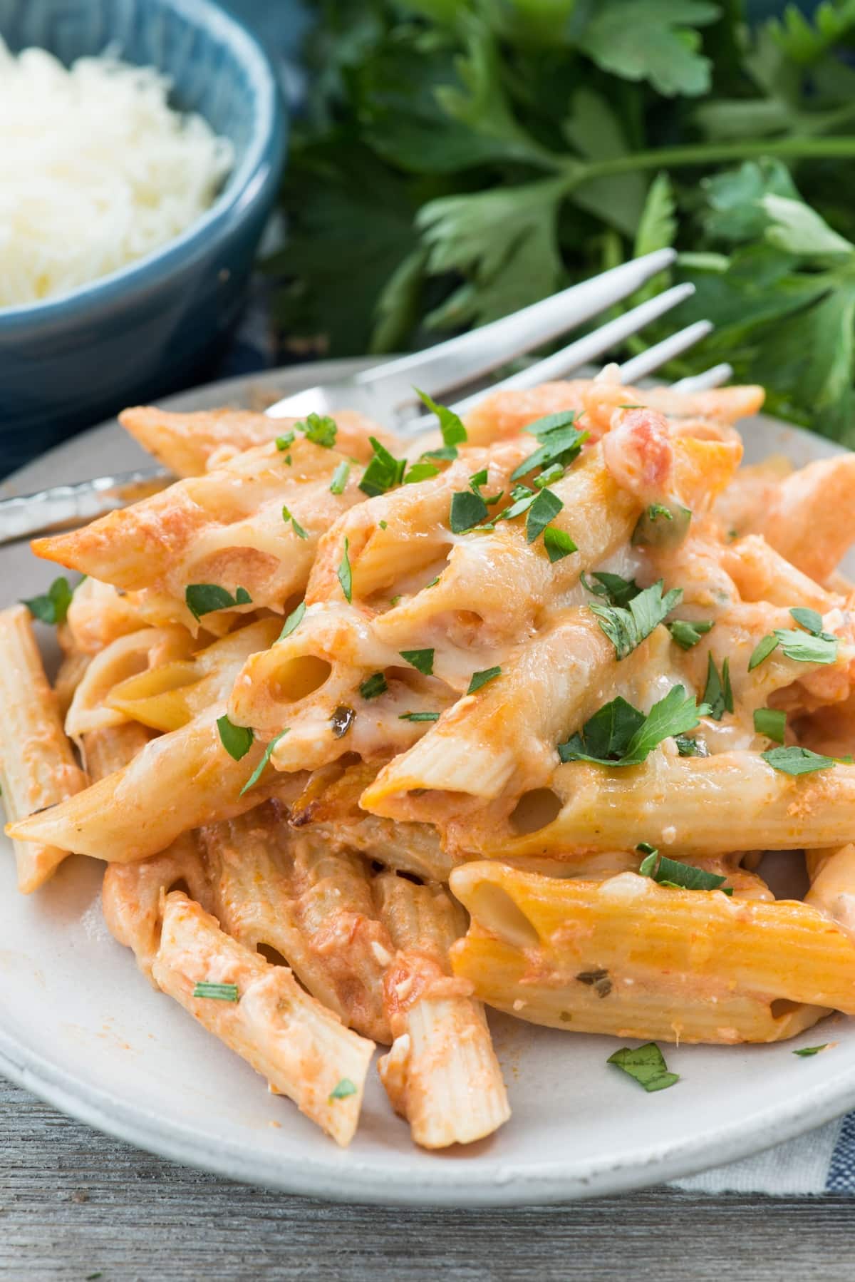 baked penne piled on a grey plate next to a silver fork.