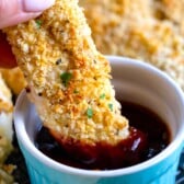 hand holding a chicken tender being dipped in BBQ sauce in a blue bowl.