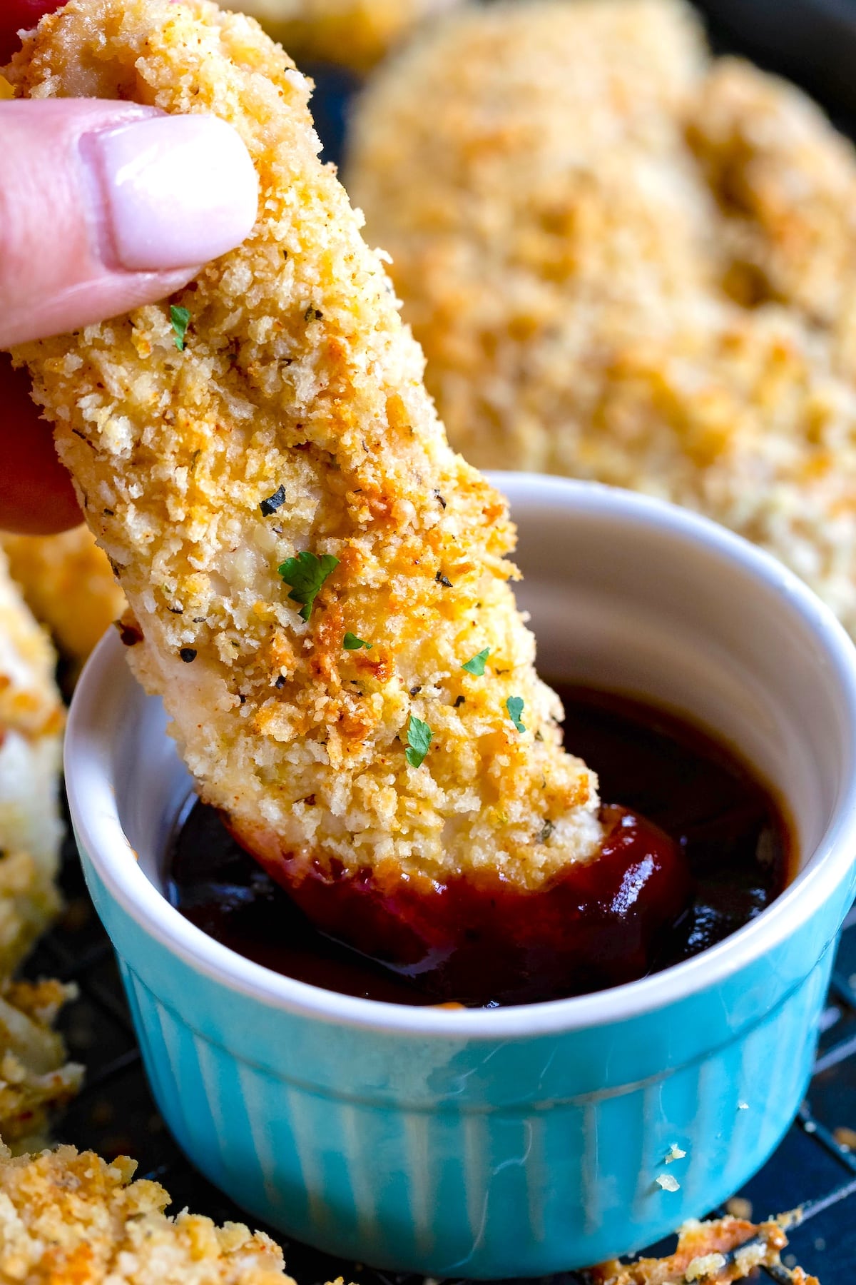 hand holding a chicken tender being dipped in BBQ sauce in a blue bowl.