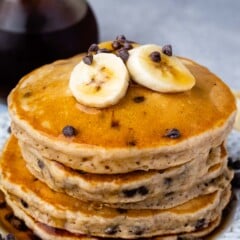 stack of banana pancakes with chocolate chips and syrup on white plate