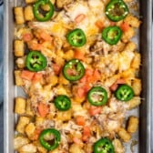 tater tots and chicken and jalapeños on a grey pan.