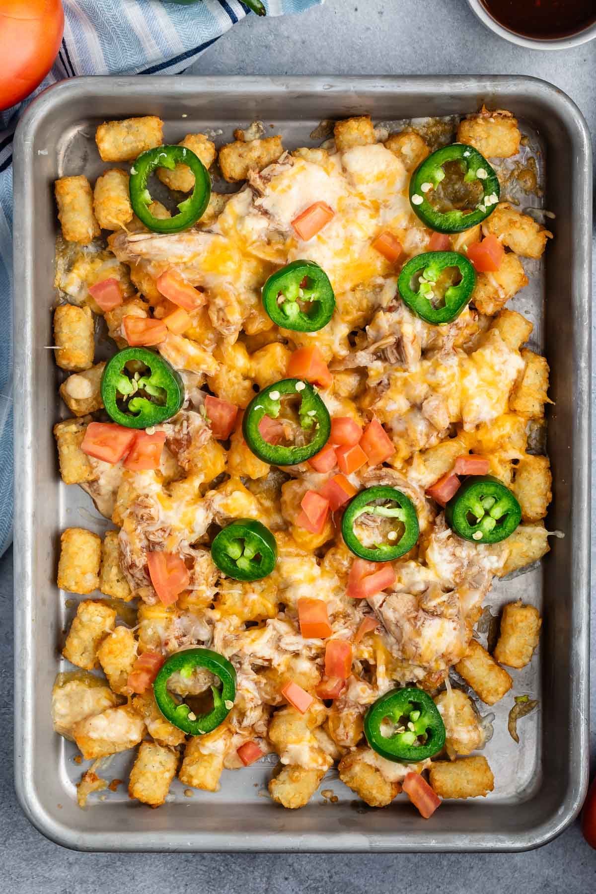 tater tots and chicken and jalapeños on a grey pan.