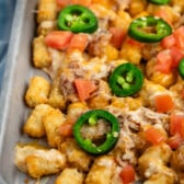 tater tots and chicken and jalapeños on a grey pan.