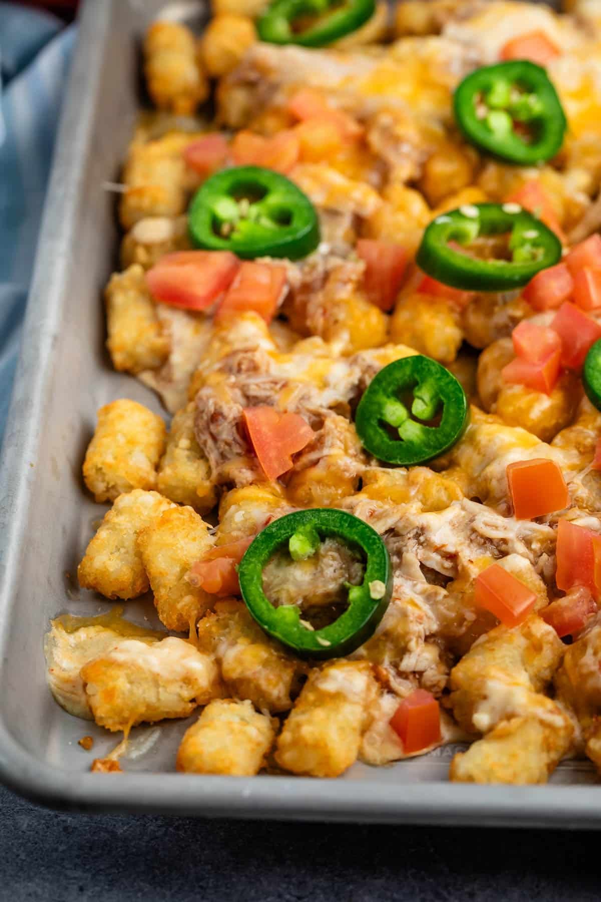 tater tots and chicken and jalapeños on a grey pan.