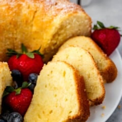 sliced pound cake on a white plate next to strawberries and blueberries.