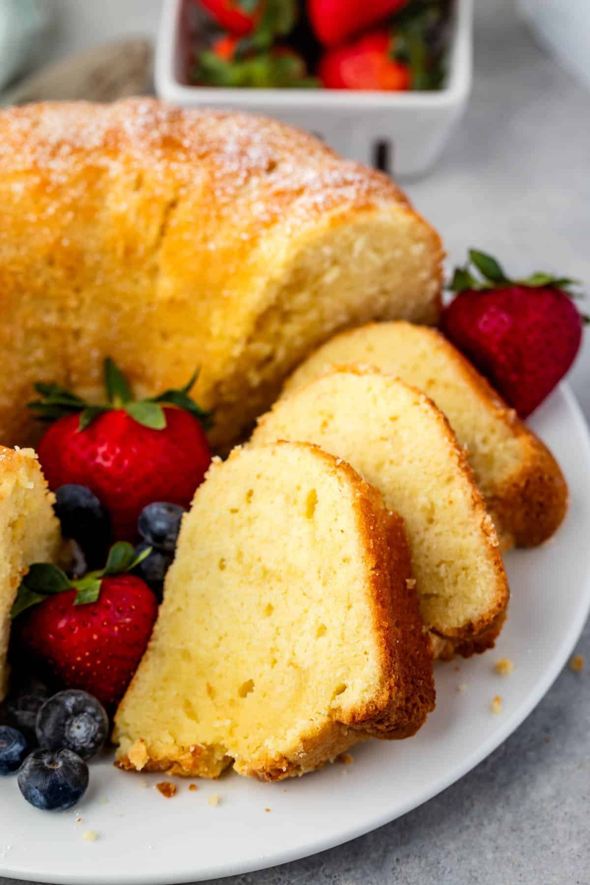 sliced pound cake on a white plate next to strawberries and blueberries.