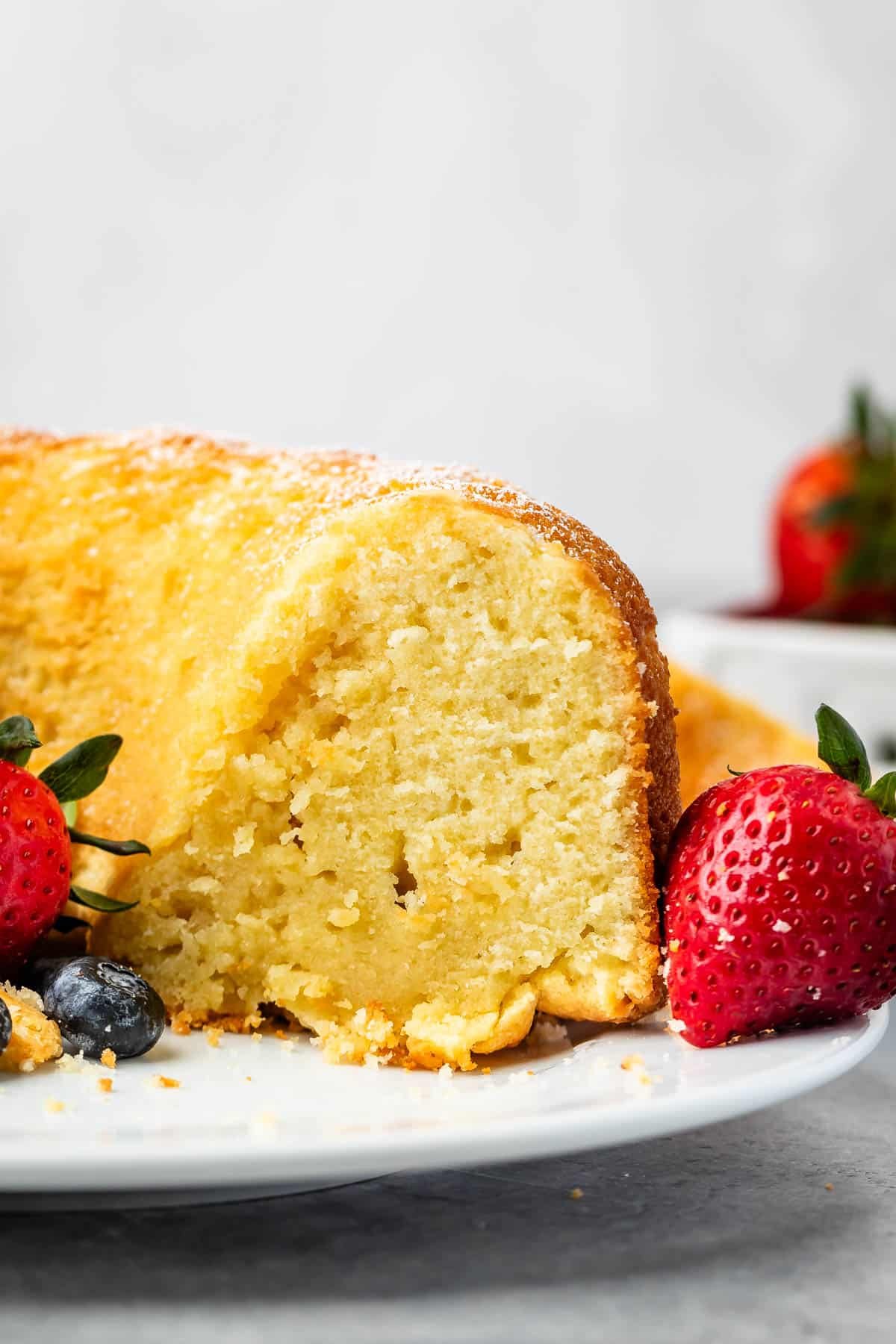 sliced pound cake on a white plate next to strawberries and blueberries.