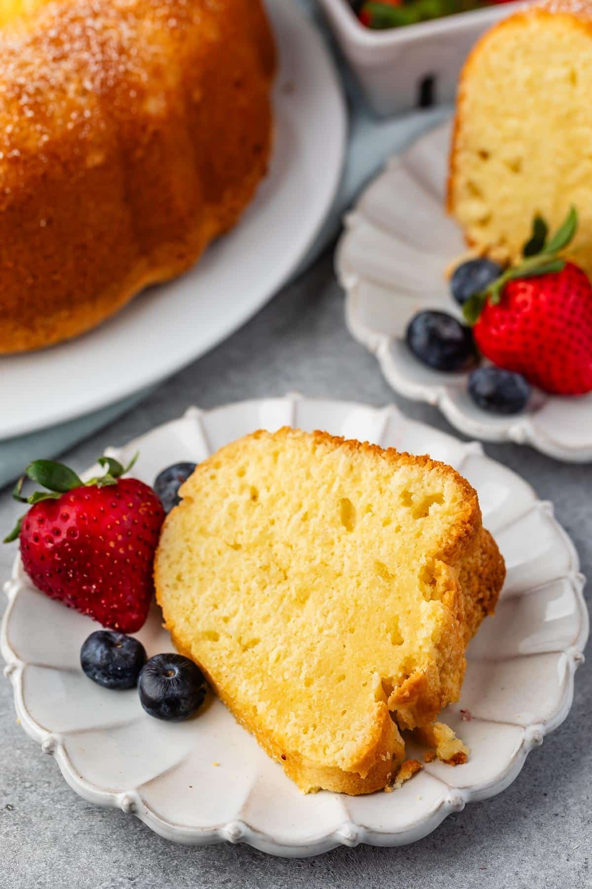 sliced pound cake on a white plate next to strawberries and blueberries.