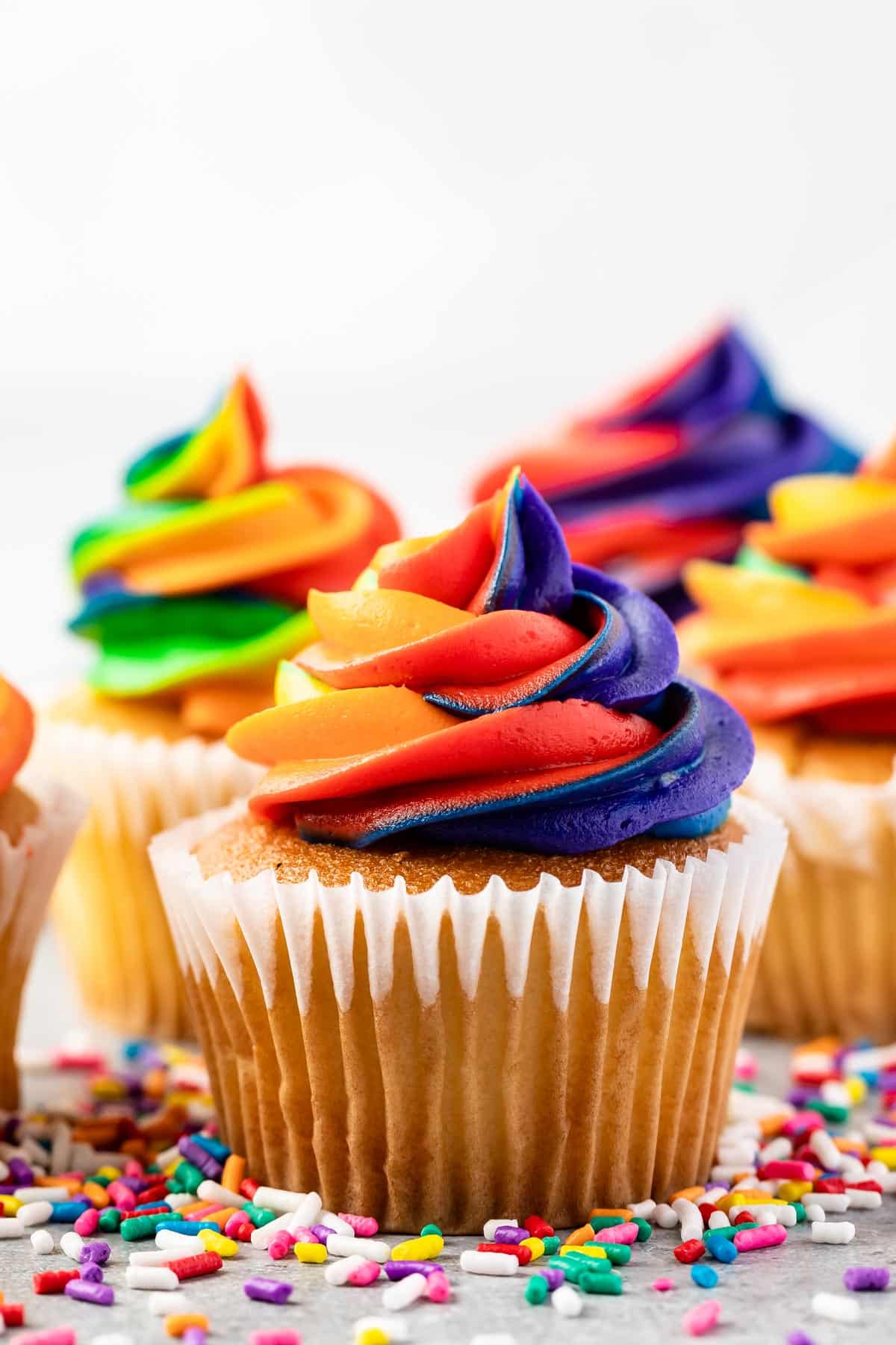 vanilla cupcakes with rainbow colored frosting on top.