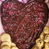 nutella spread on a pink board in the shape of a heart with candy and cookies around the edge.