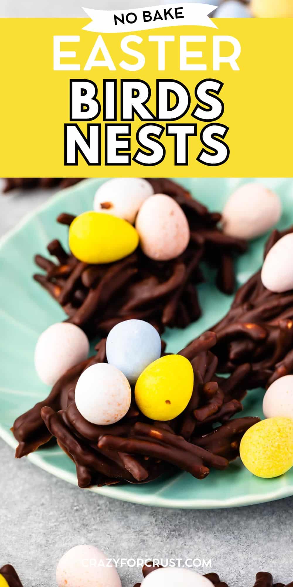 A plate of no-bake chocolate birds nest cookies topped with pastel-colored candy eggs, placed on a light green dish with a yellow banner above reading Easter Birds Nests.