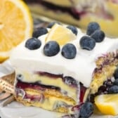 square slice of cake with blueberries and lemons on top.