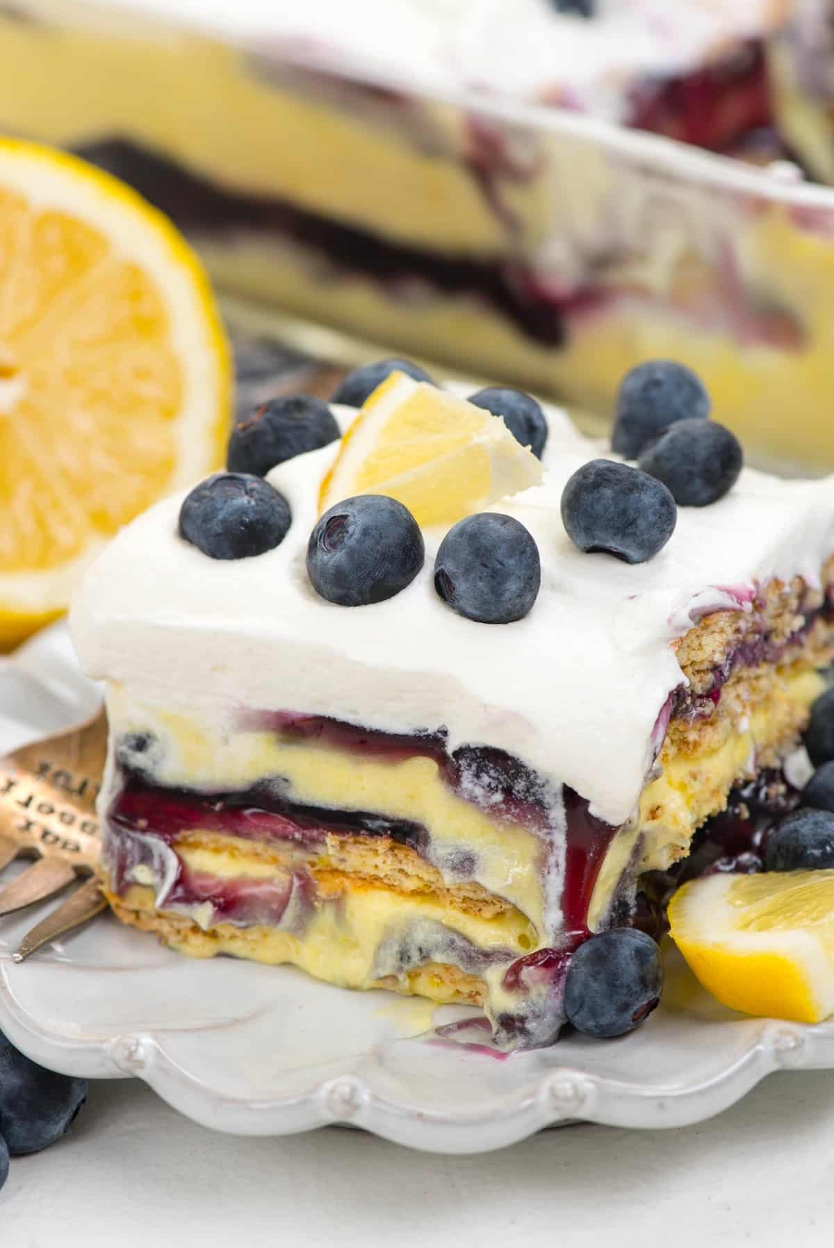 square slice of cake with blueberries and lemons on top.