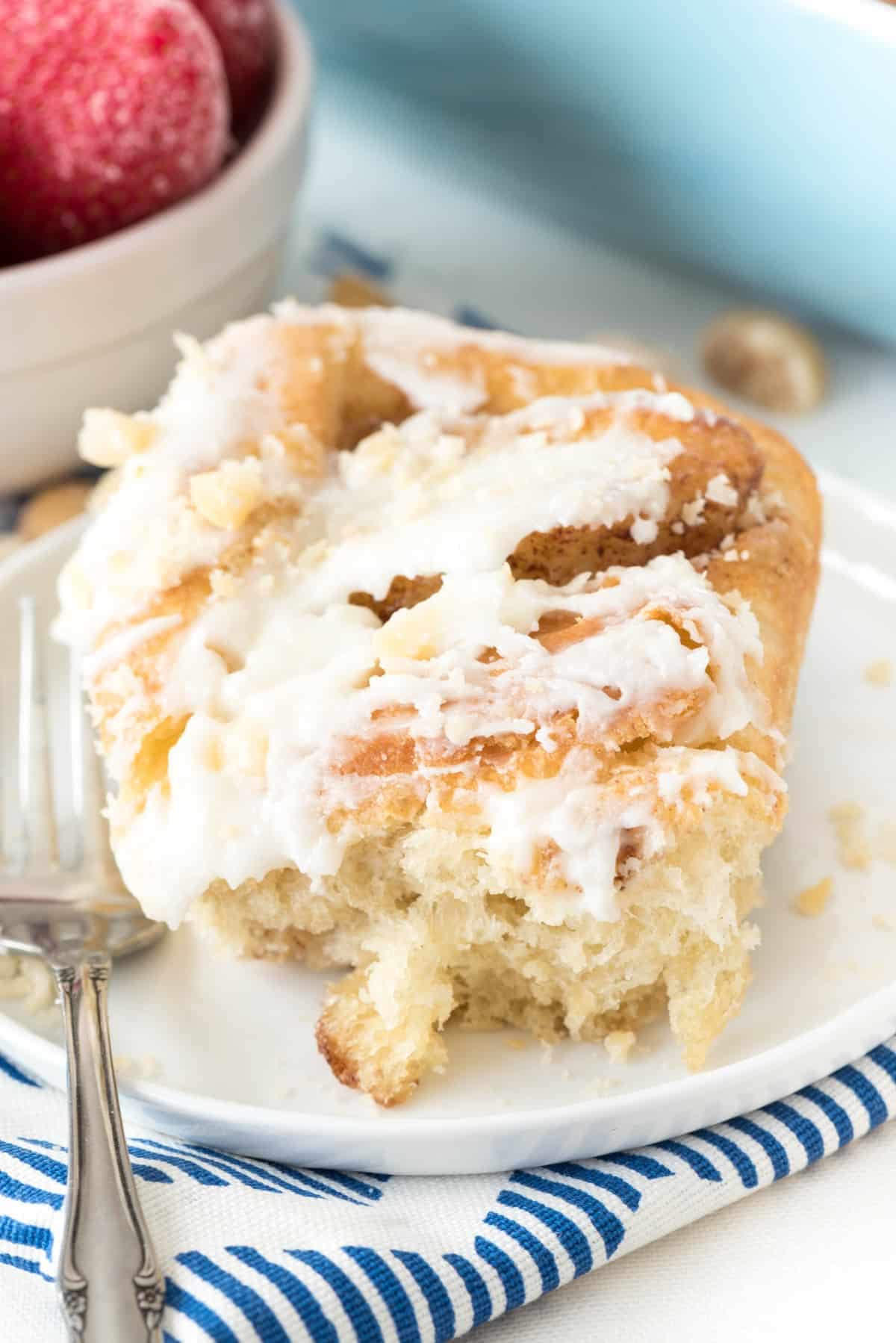 one cinnamon roll on a white plate with a fork.