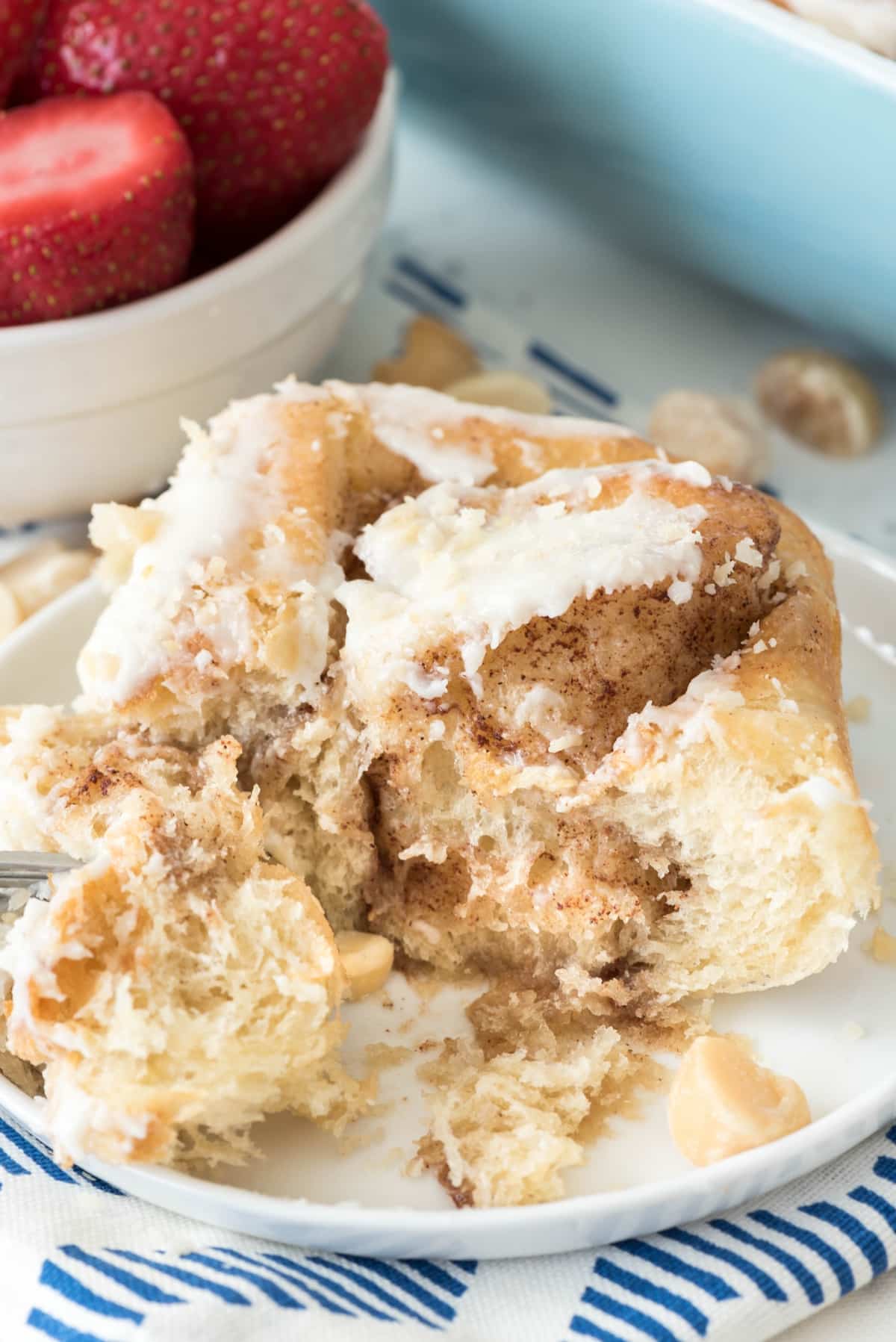 one cinnamon roll on a white plate with a fork.