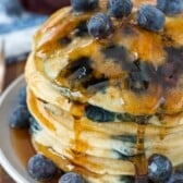 stacked pancakes with blueberries baked in and covered in syrup.